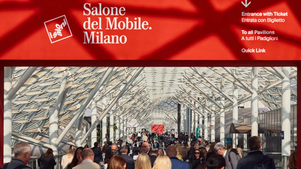 Banner oficial vermelho do 'Salone del Mobile Milano' com logo iSaloni e informações de acesso bilíngue sobre entrada com ticket e pavilhões.